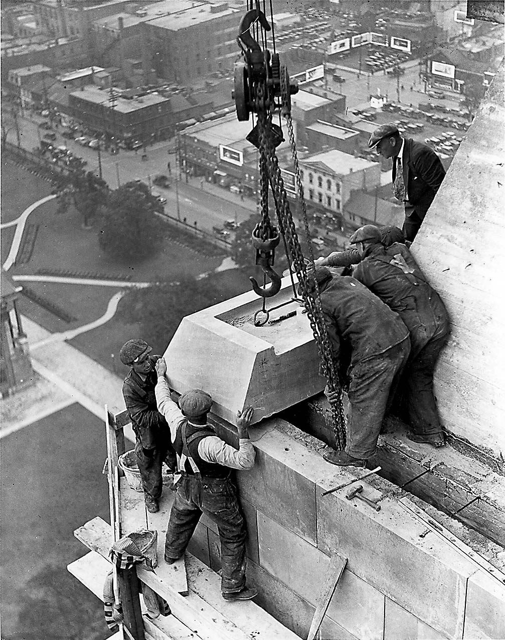 Photograph. “Raising last stone to top of Canada Life Building in Toronto, Ontario, Canada. The image background shows the older lower-rise shops and businesses along Queen Street West, demonstrating the transition of Toronto’s downtown in the early 20th century from a low-rise commercial district to a high-rise office centre.”