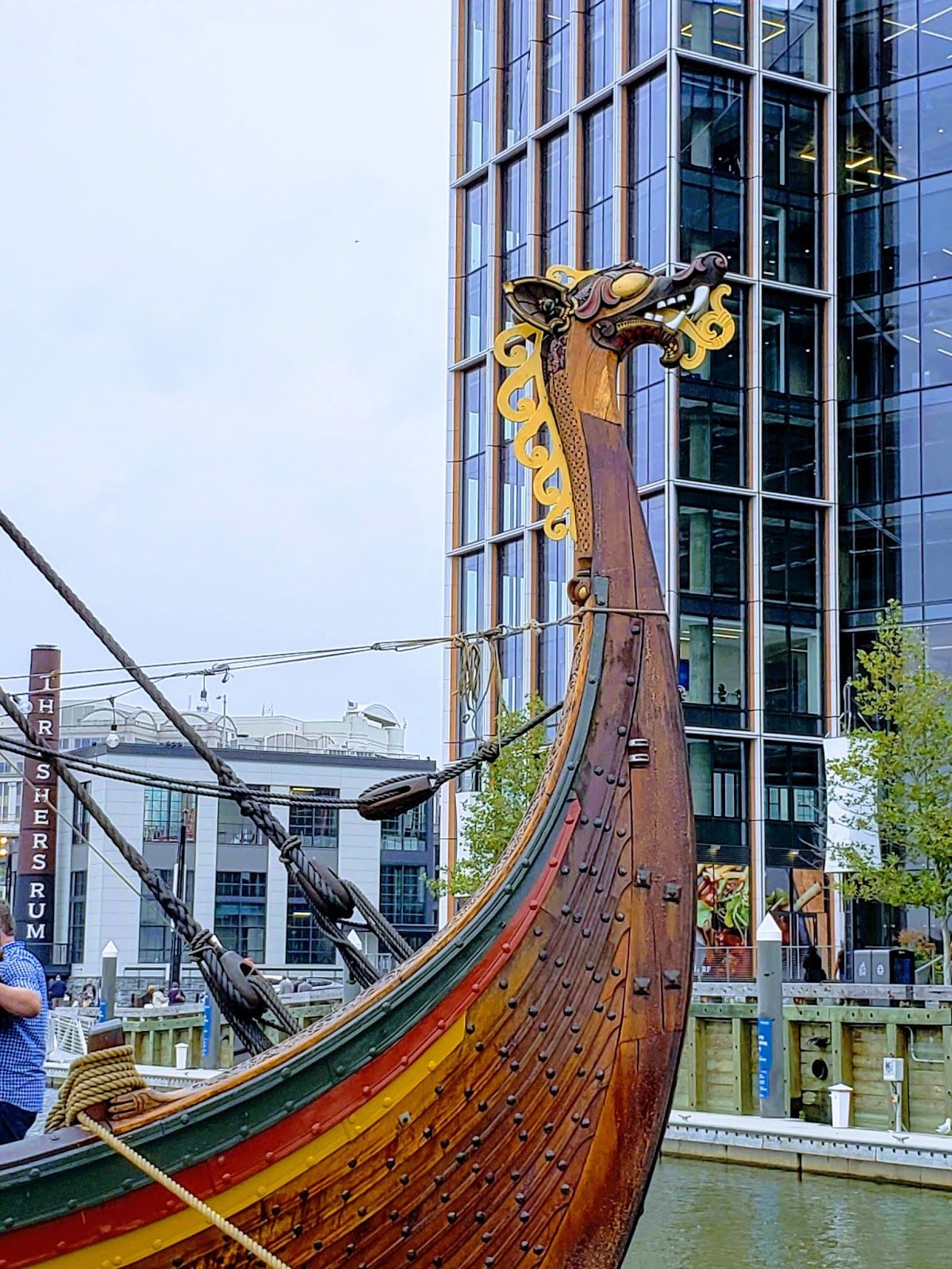 The prow of a wooden Viking boat rises up in the foreground of the picture, adorned with a golden dragon head. In the background, water, then a modern glass skyscraper, and a smokestack advertising Thrasher’s Rum. (It’s nice rum if you get the chance.)