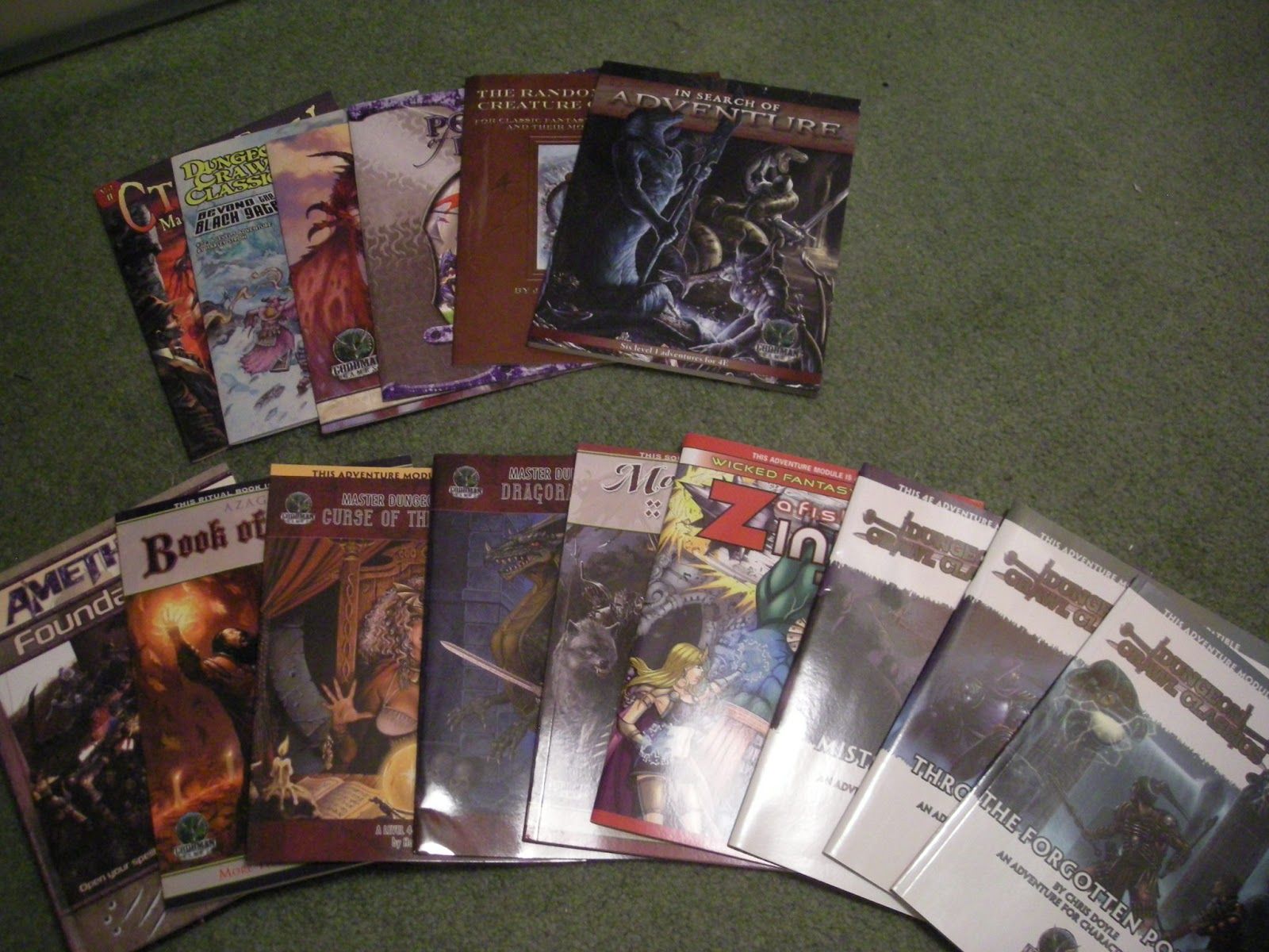 Two rows of letter-sized paperback RPG supplements, spread out on a green carpet.