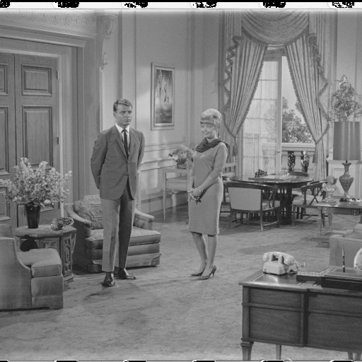 A woman in a long dress and a man in a suit stand idly in the middle of a large room. In the foreground a phone sits on a desk, behind them curtained double doors open onto a balcony. Around them are various chairs, tables, lamps, and flowers. Along the top and bottom edges, a harsh black and white “film strip” pattern is visible.