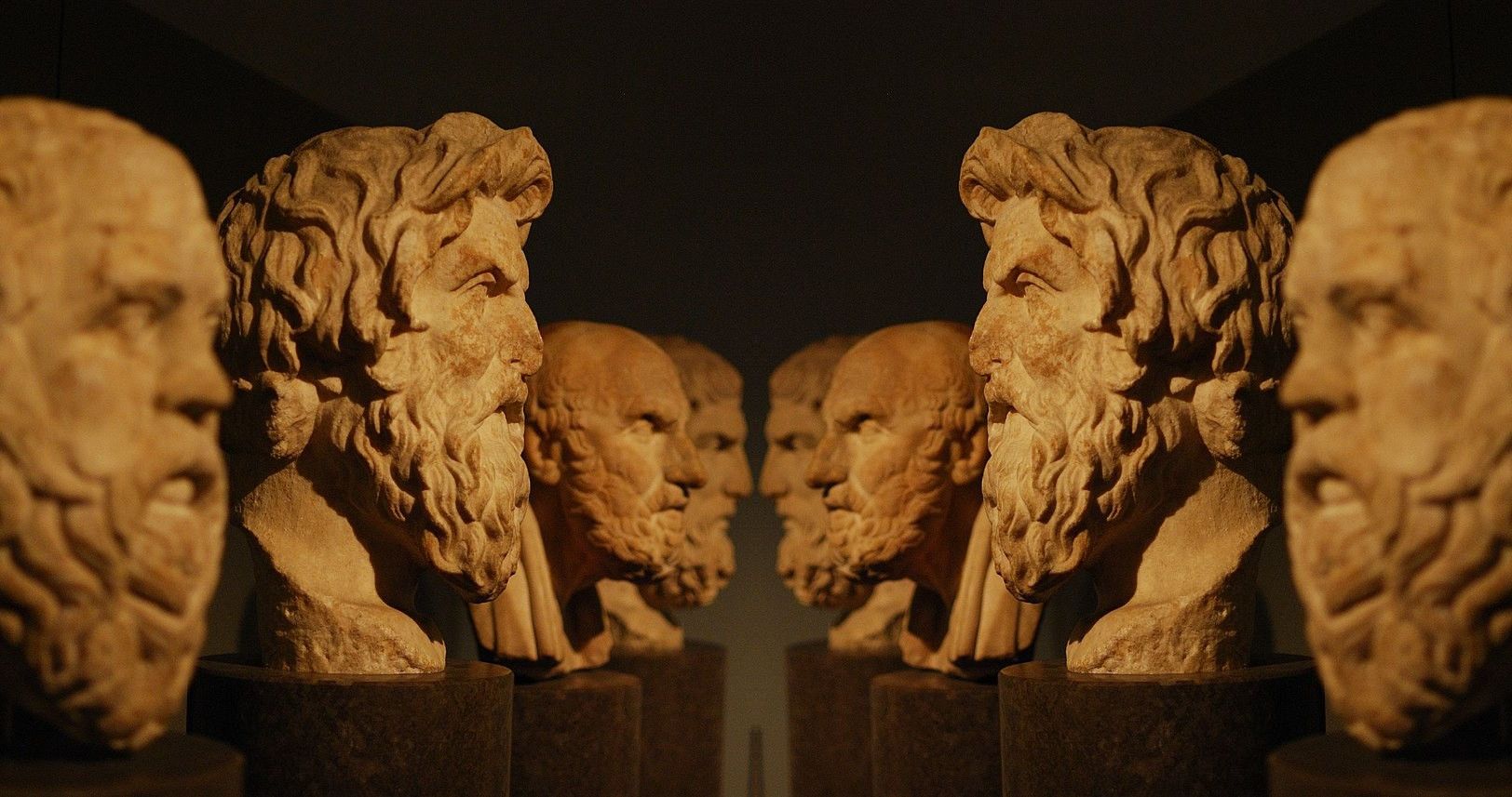 A row of weathered stone busts of ancient Greek philosophers is mirrored across the center, like two teams staring each other down before a fight.