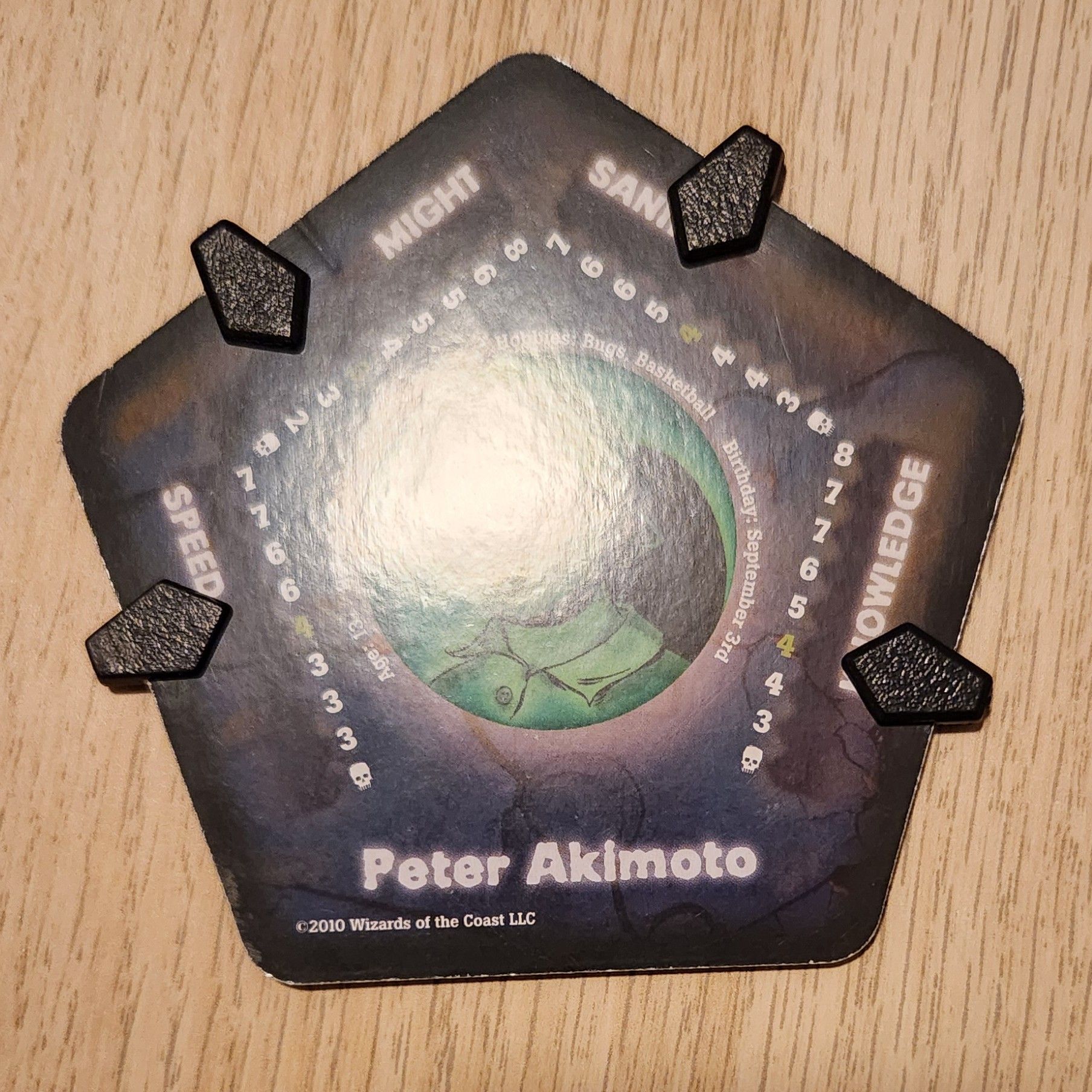 A pentagonal card named “Peter Akimoto,” the central illustration obscured by glare. Along the top four edges, trackers point to different numbers along scales for Speed, Might, Sanity, and Knowledge.