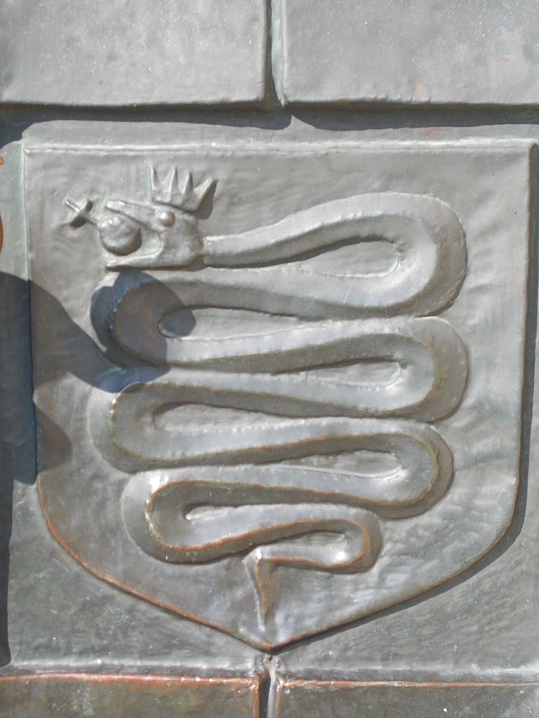 A crest in stone with a coiled, crowned snake, holding a fruit in its mouth.