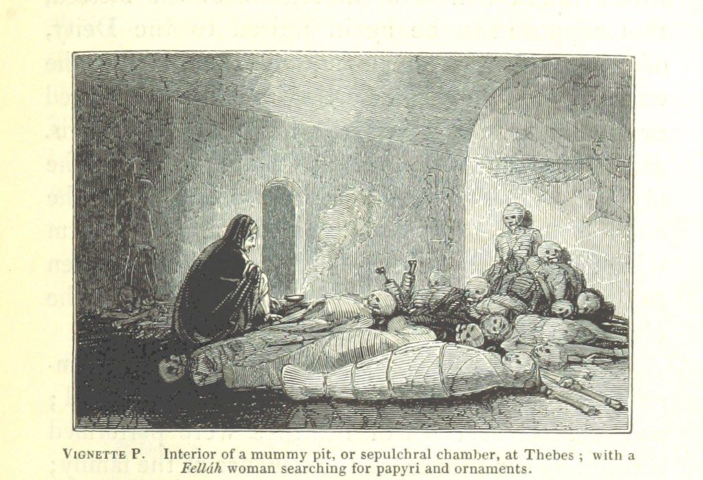 Black and white illustration of a pile of pale, bundled bodies in a room with one woman in a black cloak. Caption: “Interior of a mummy pit, or sepulchral chamber, at Themes; with a Fellúh woman searching for papyri and ornaments.”