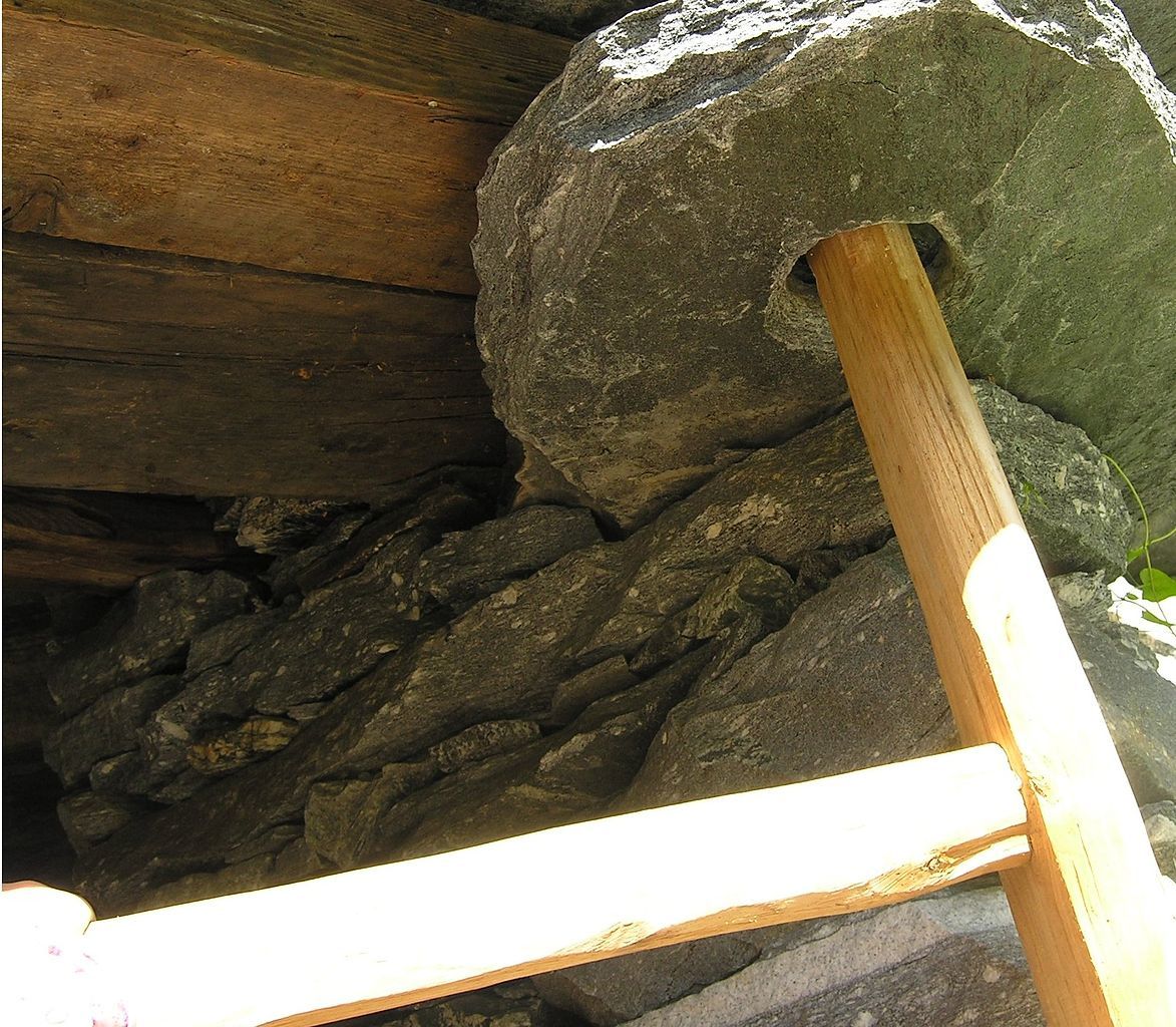 A close-up of the construction of a pivot hinge: a vertical wooden post extends above a horizontal wooden frame, into a stone recess in the ceiling.