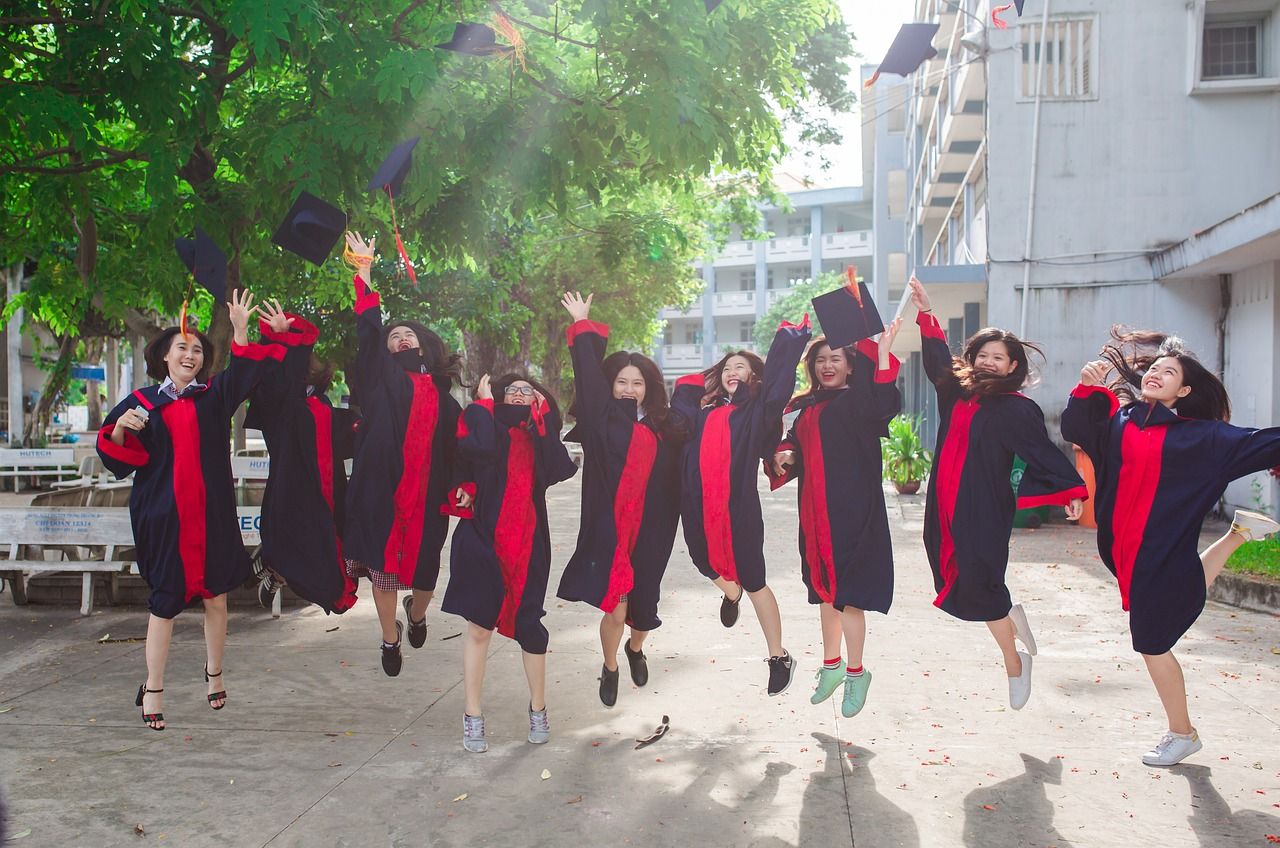 Nine young women in long back-and-red robes leap into the air while throwing their mortarboard hats.