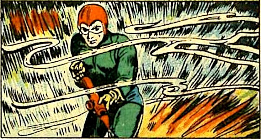 A man in a tight green suit and red helmet with goggles holding a red spraying device. The foreground is wisps of smoke and the background is raging flames.