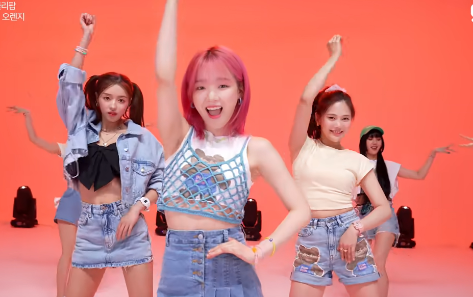 picture of YooA, Seunghee, and Hyojung dancing, their right arms raised to the ceiling, Seunghee in front, against an orange background