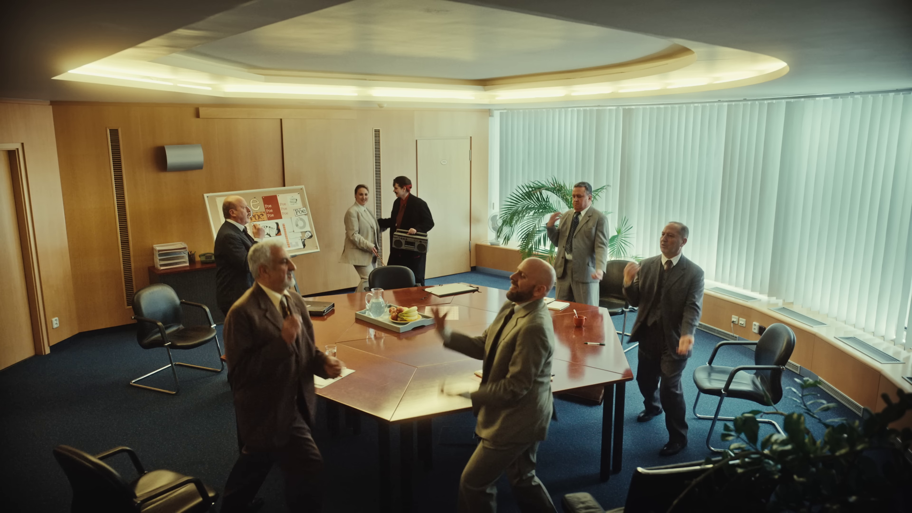 image of a bunch of men in suits dancing around a wide table while Teya and Salena look on