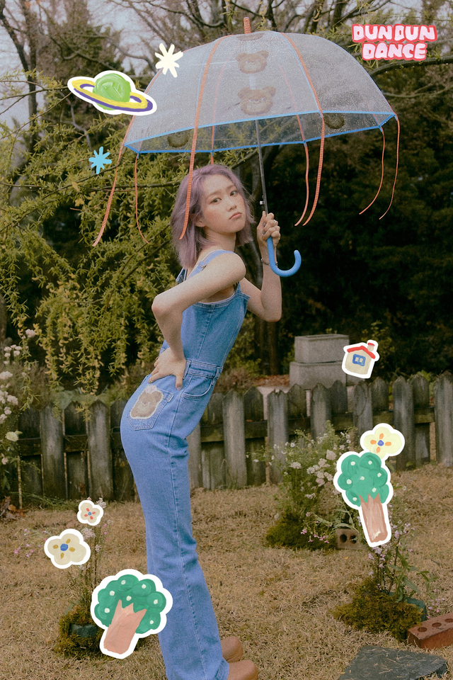 picture of Jiho wearing overalls, turned to the side, holding an umbrella, with her hand on her hip
