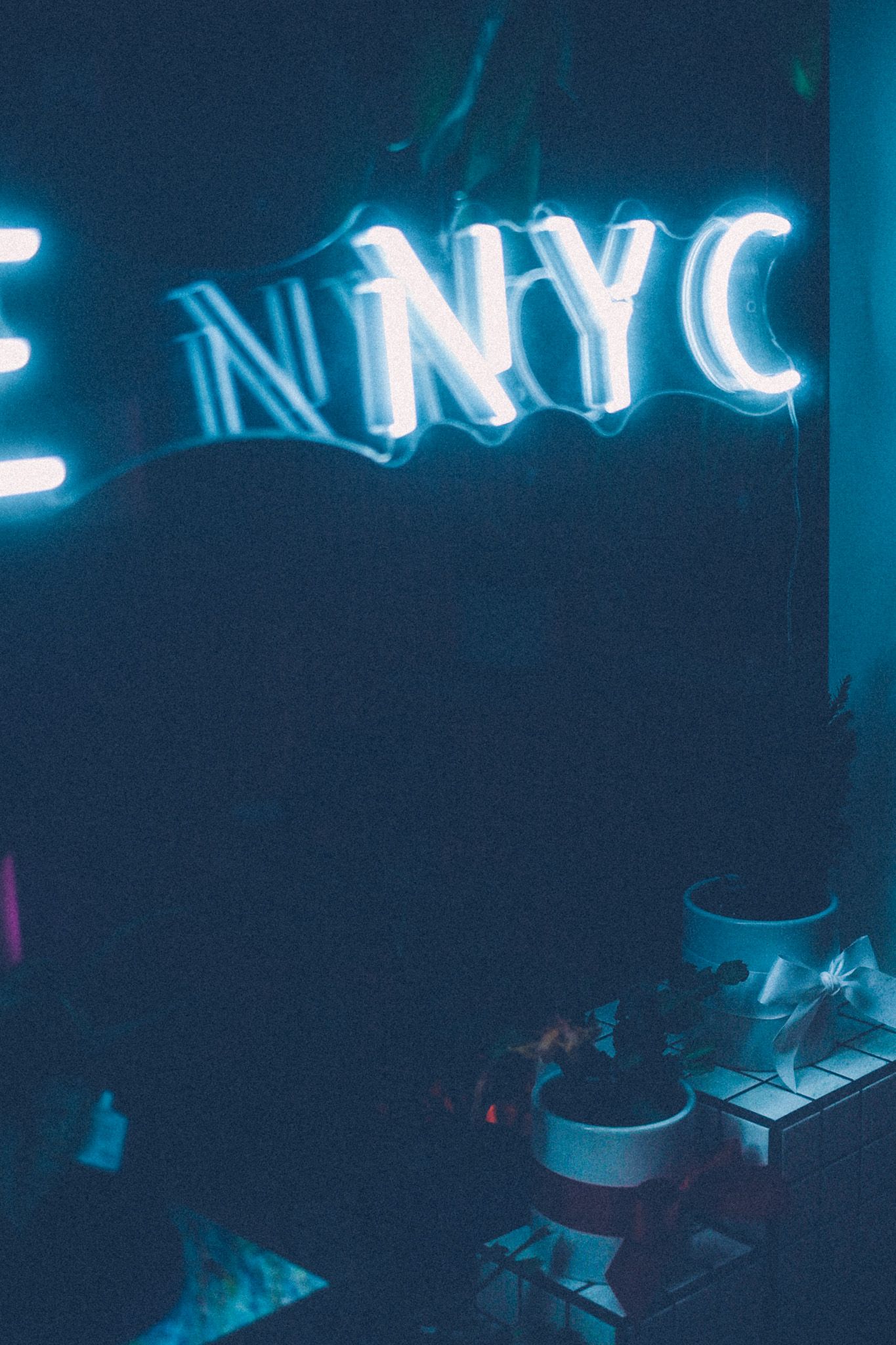 A white-blue neon sign saying NYC hangs in a dark store window.