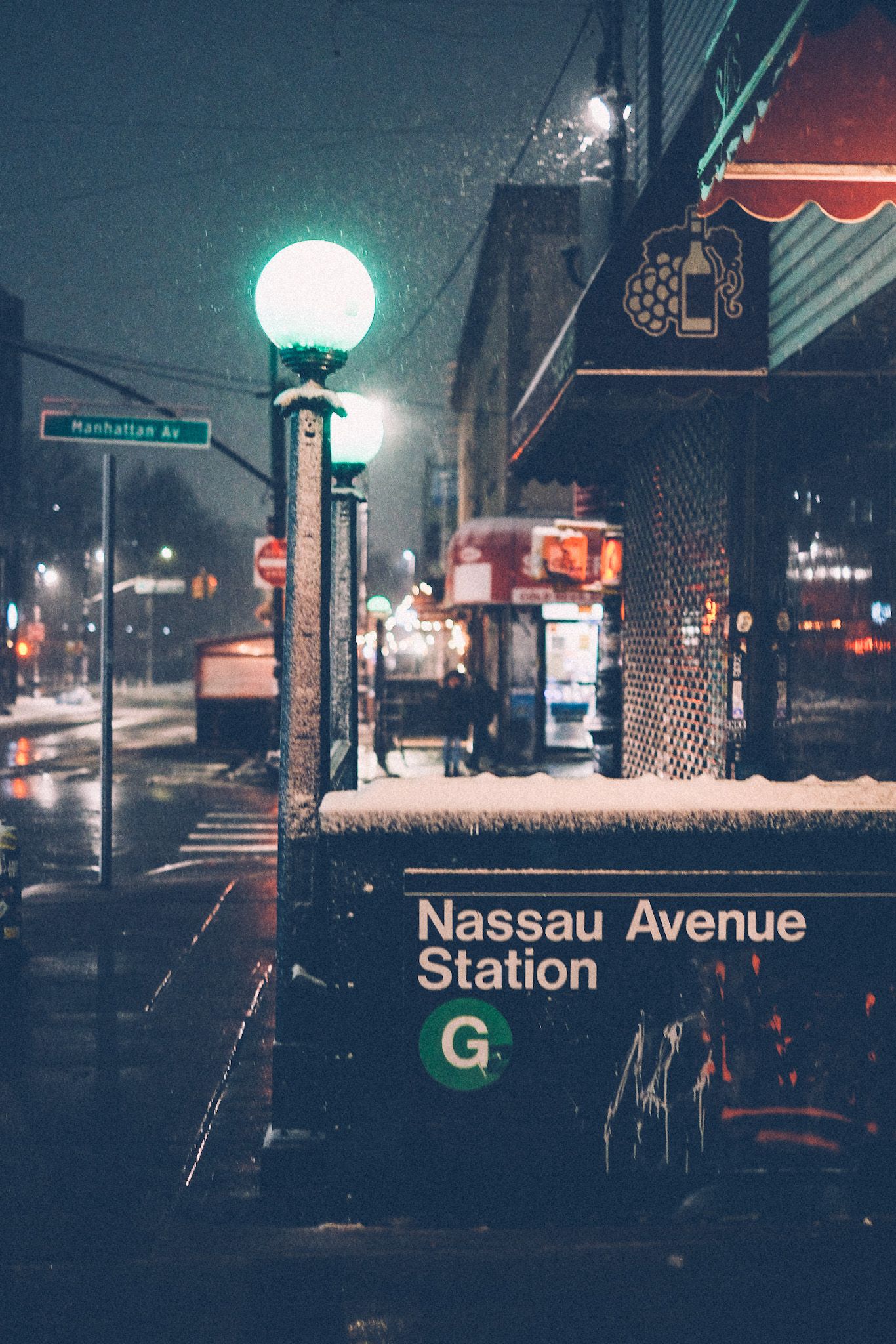 A pair of green NYC subway lamps illuminate the Nassau Avenue station on a snowy night in Brooklyn.