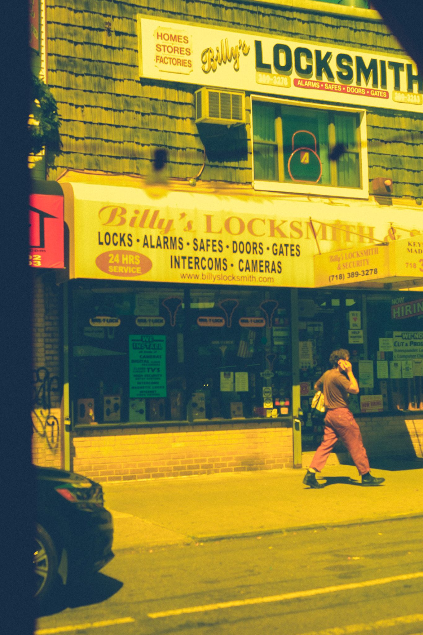 Through a yellow pane of plastic, a man walks down a street past a locksmith shop.