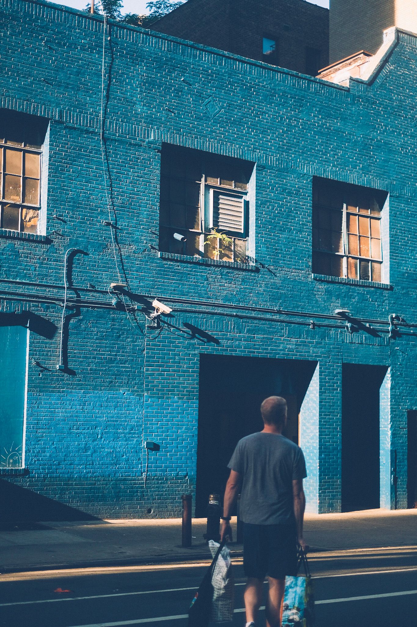 A man walks in front of the camera toward a blue brick building lit with morning sun.