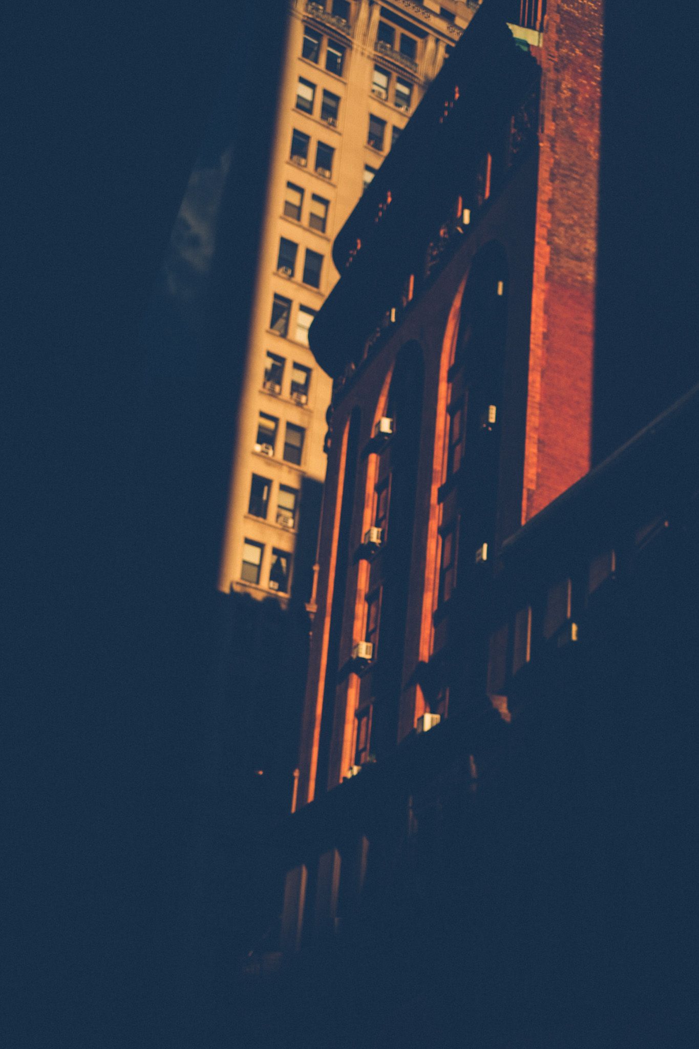 Amid harsh shadows near sunset, tall red brick buildings rise out of the frame.
