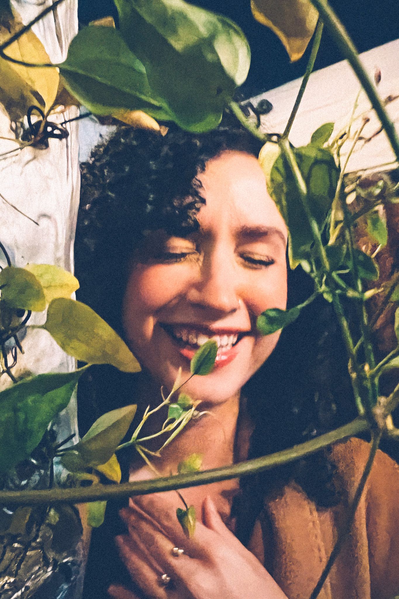 A woman grins and closes her eyes while laughing, her face framed in green fake ivy.