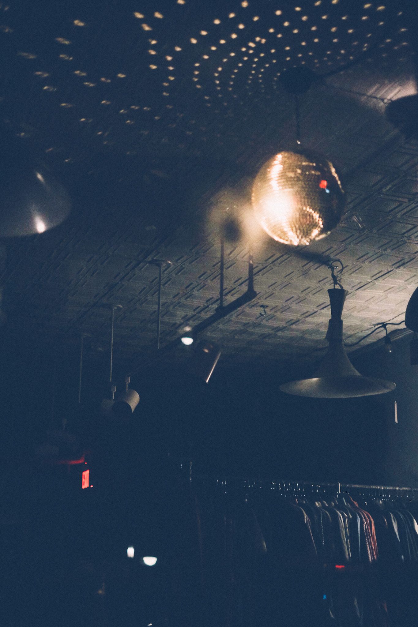 A disco ball inside of a dark department store reflects light across the ceiling, revealing racks of clothes in the background.