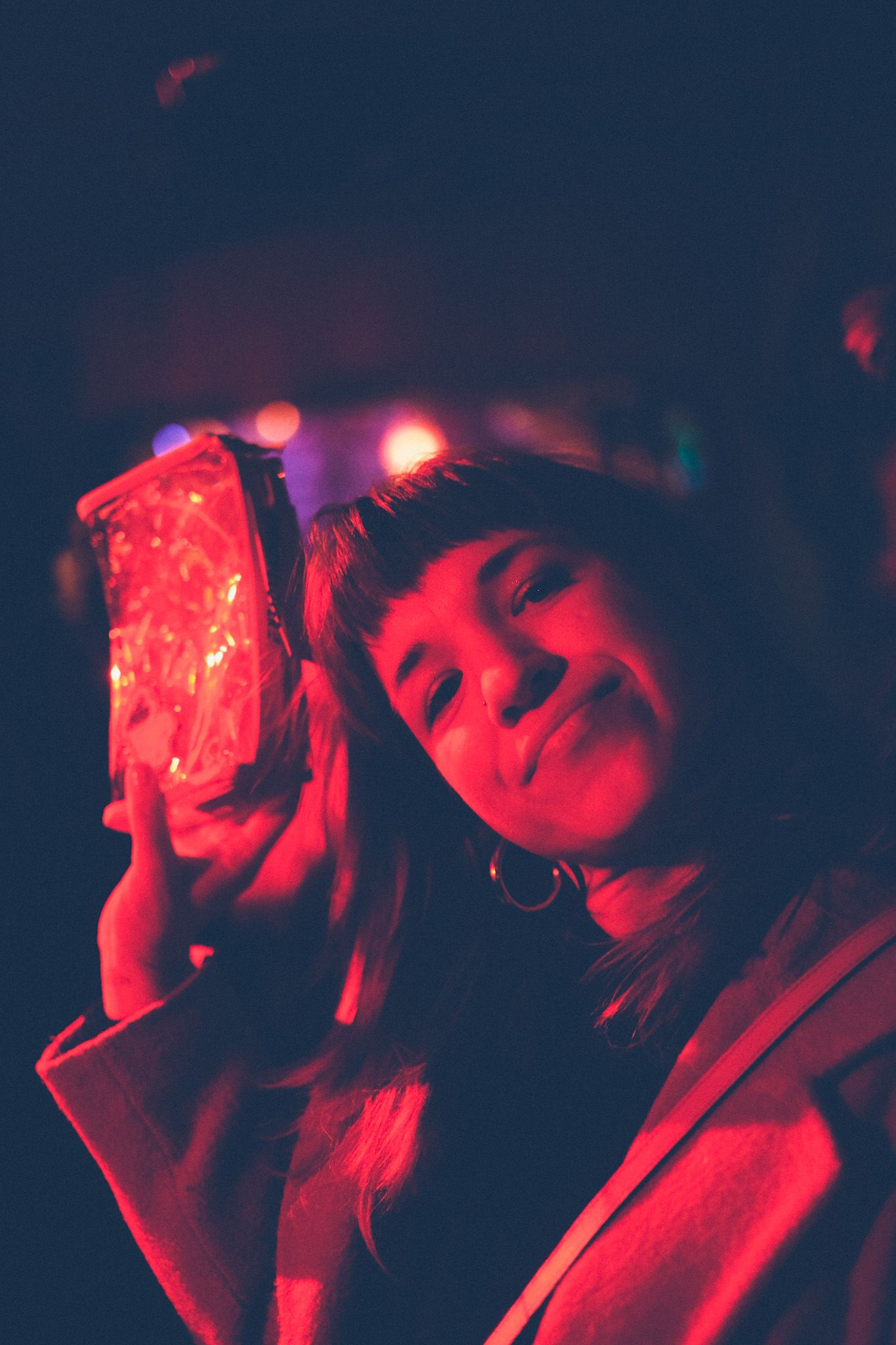A woman saturated in red light holds a bag up, looking into the camera with attitude.