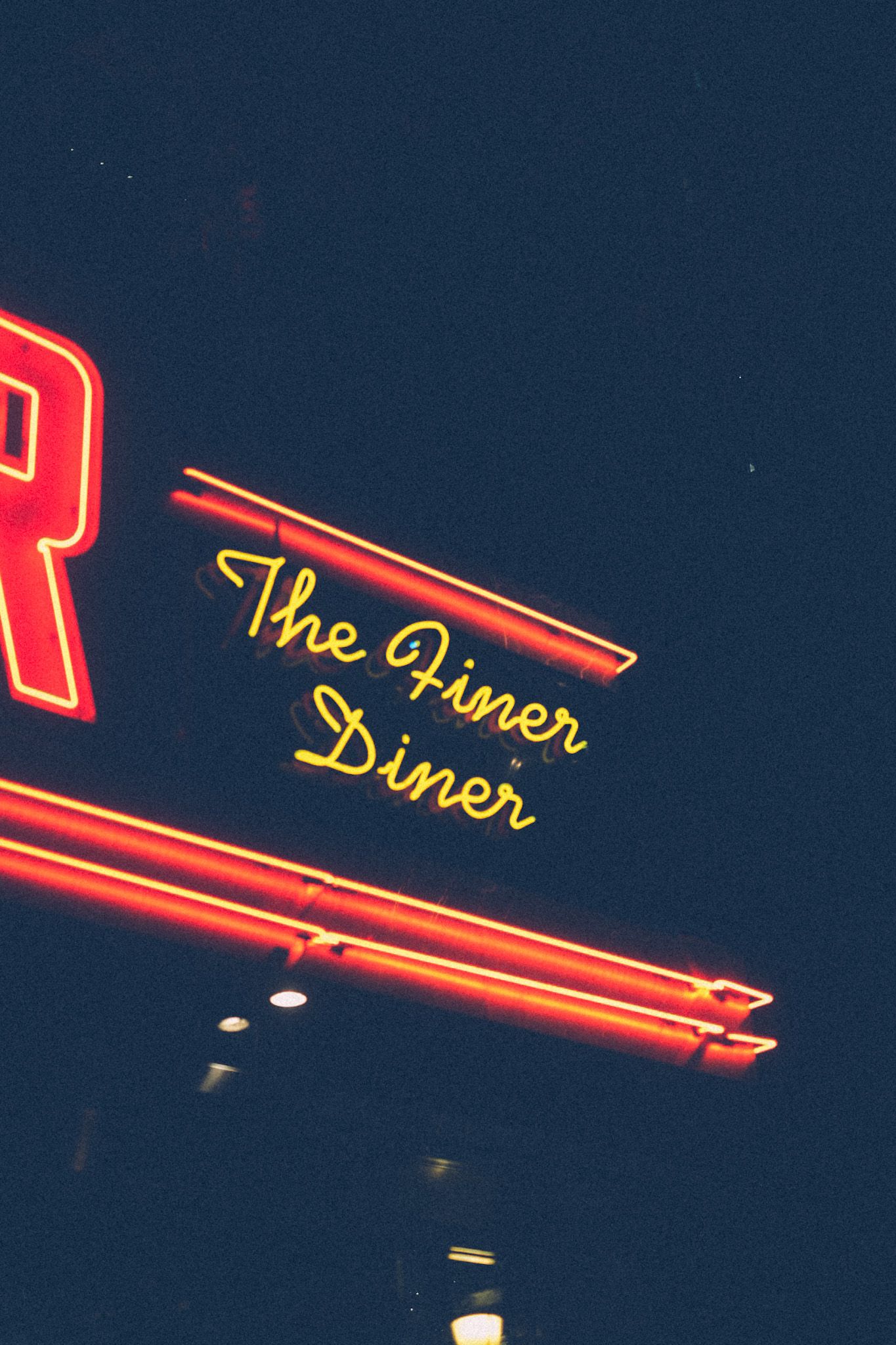 In the night, a neon sign emerges out of the bottom left of the photo, saying The Finer Diner.