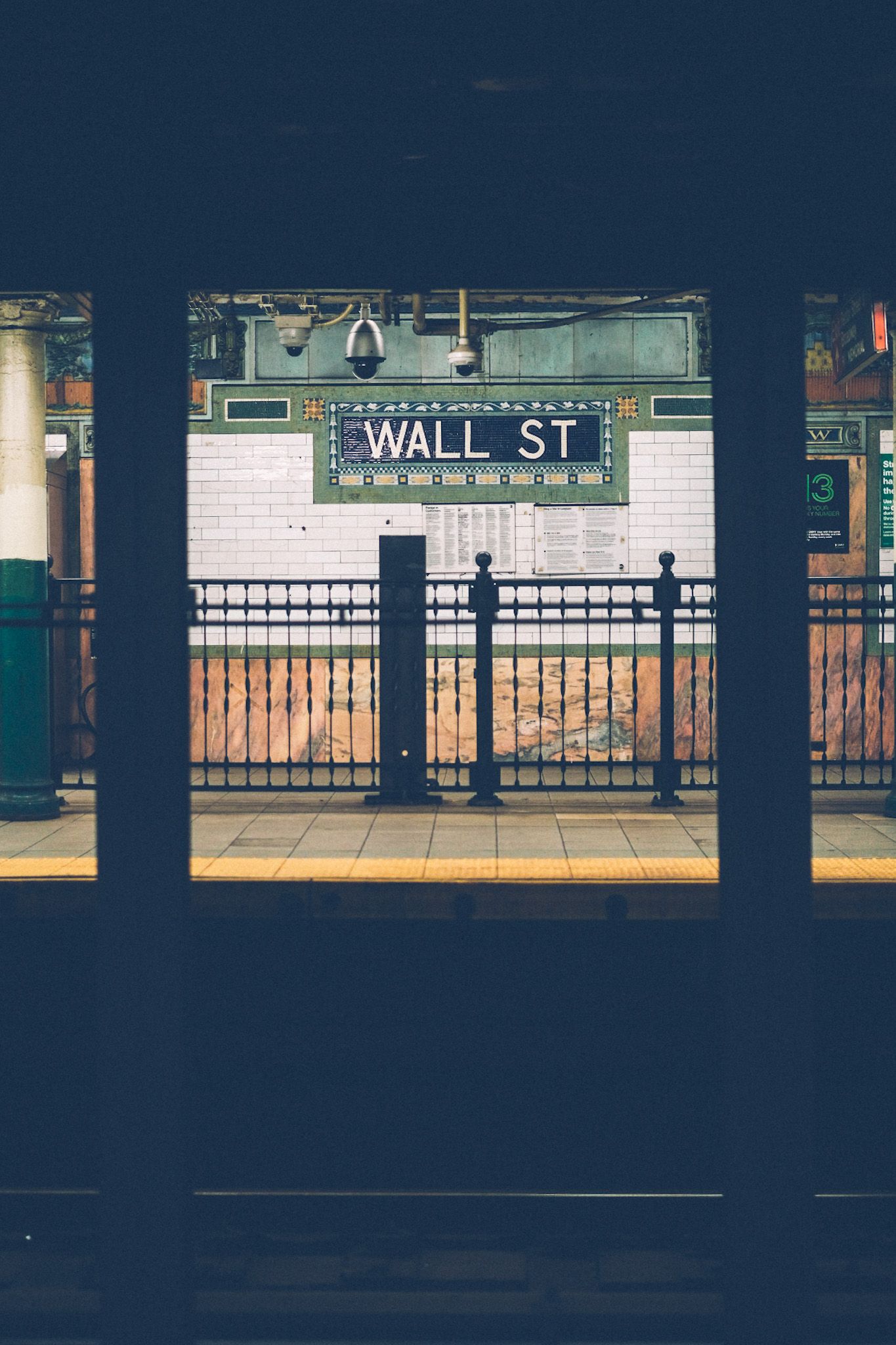 The view from a subway station across the train tracks, staring at a wall tiled with the words Wall St.