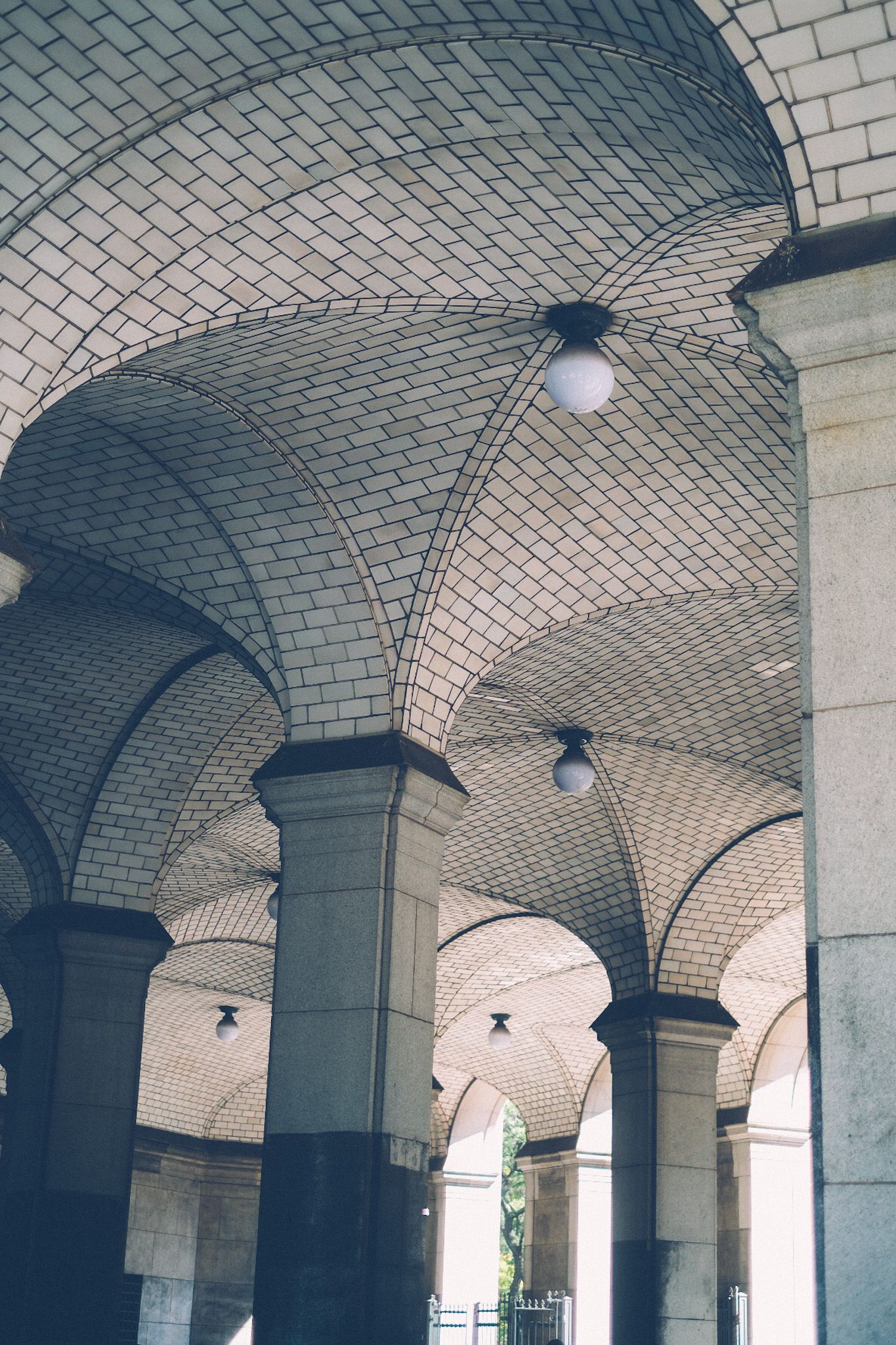 Pillars with white tile rise up to create archways, uniting as the ceiling of a subway station.