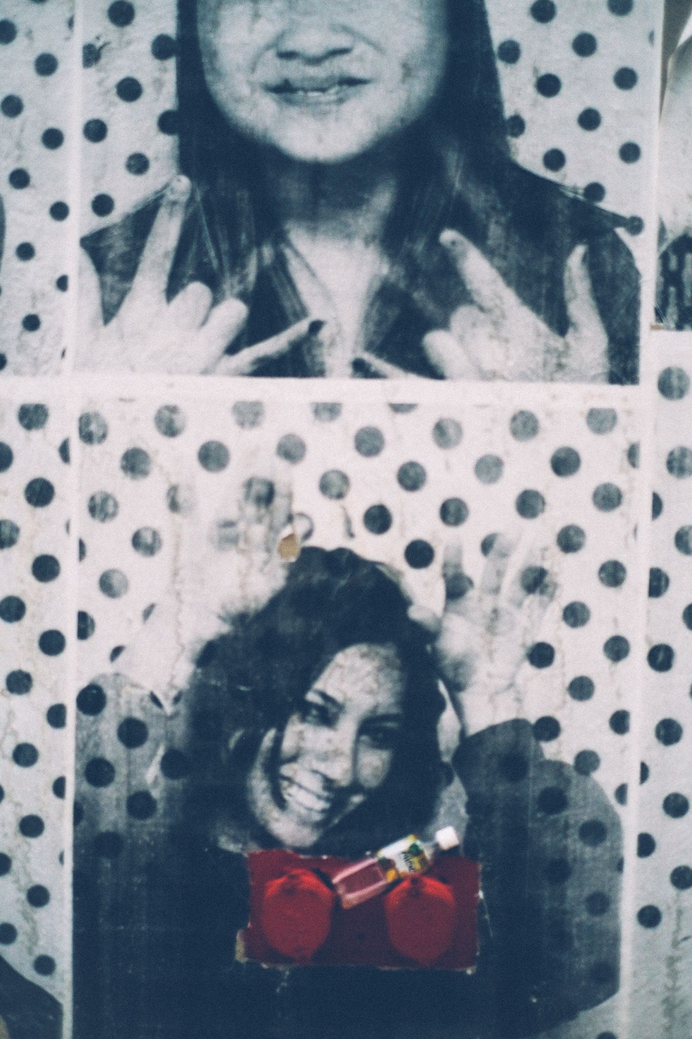 A black and white poster printed with polka dots and pictures of smiling students is pasted to a wall, behind a red Siamese water hose connector.