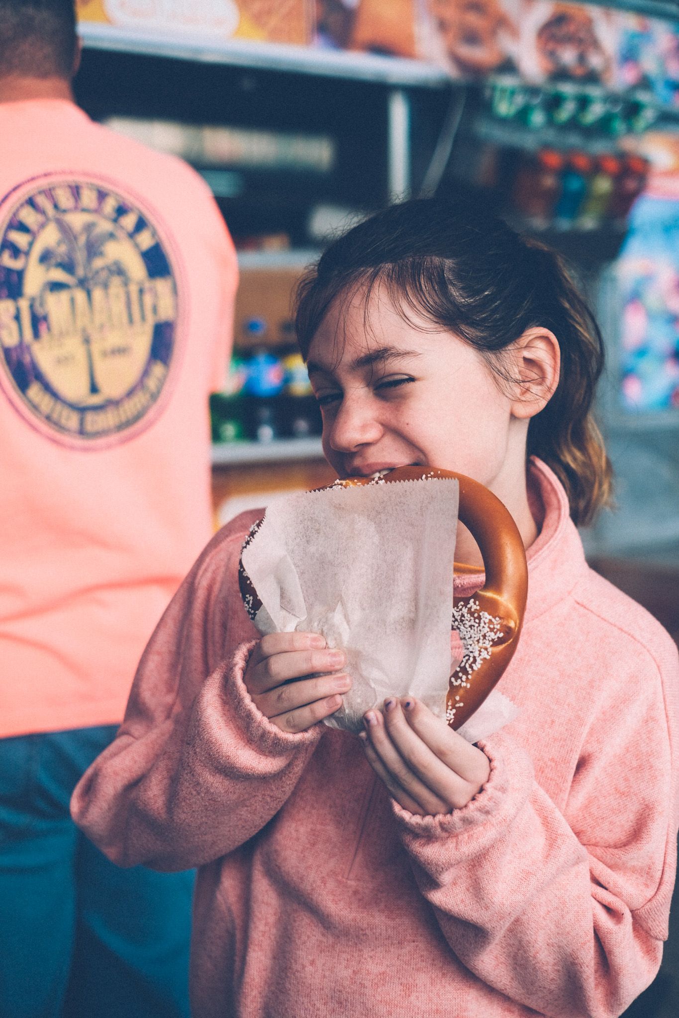 A girl eats a pretzel from a street cart.