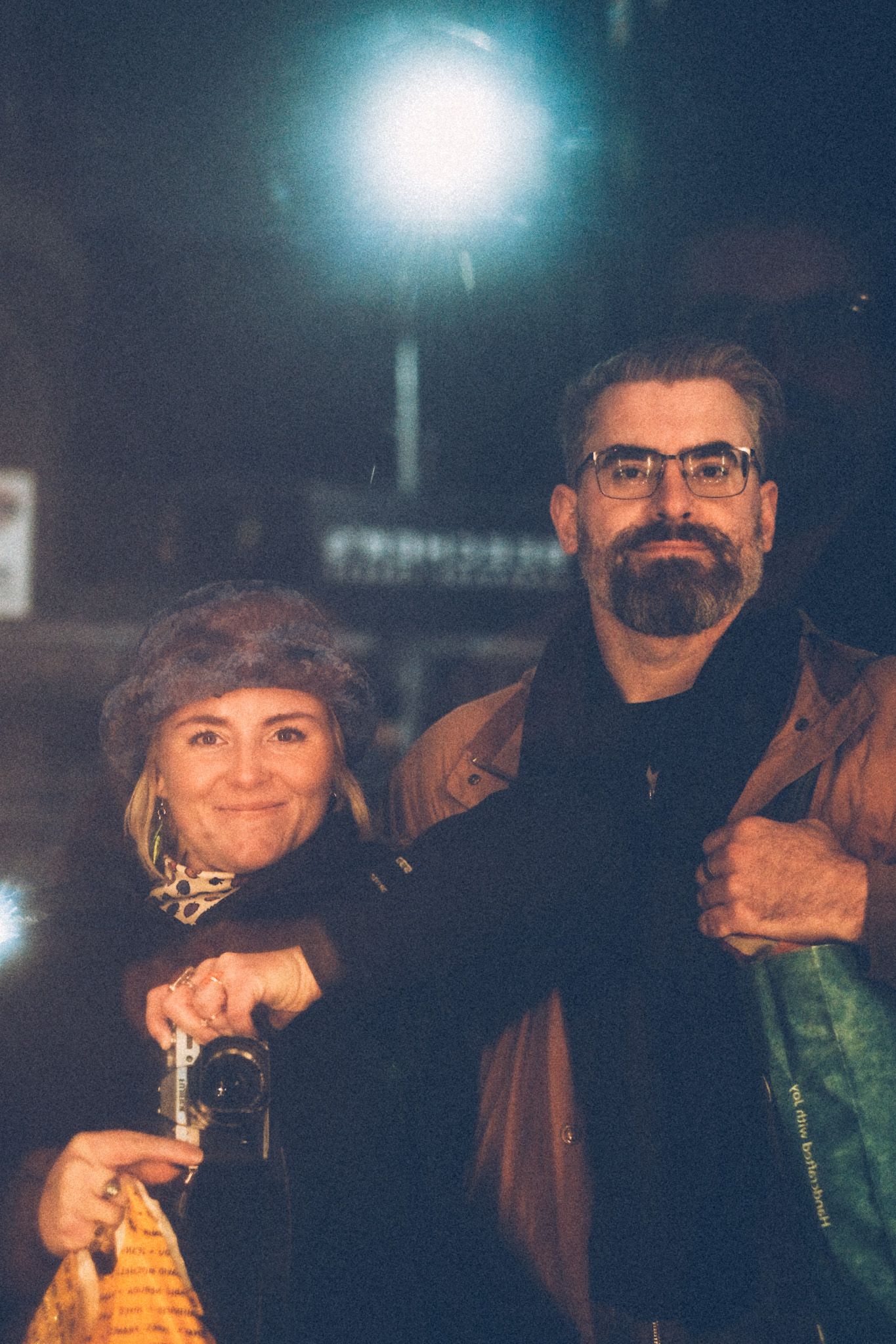 A couple takes a self-portrait in a store window at night, smiling.
