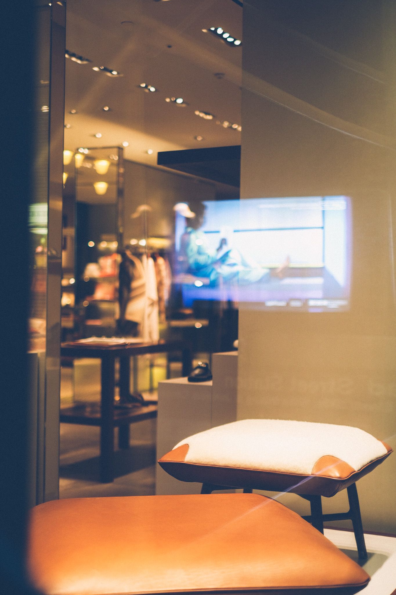 A television screen is reflected against the glass of a window display, fine seating showcased.