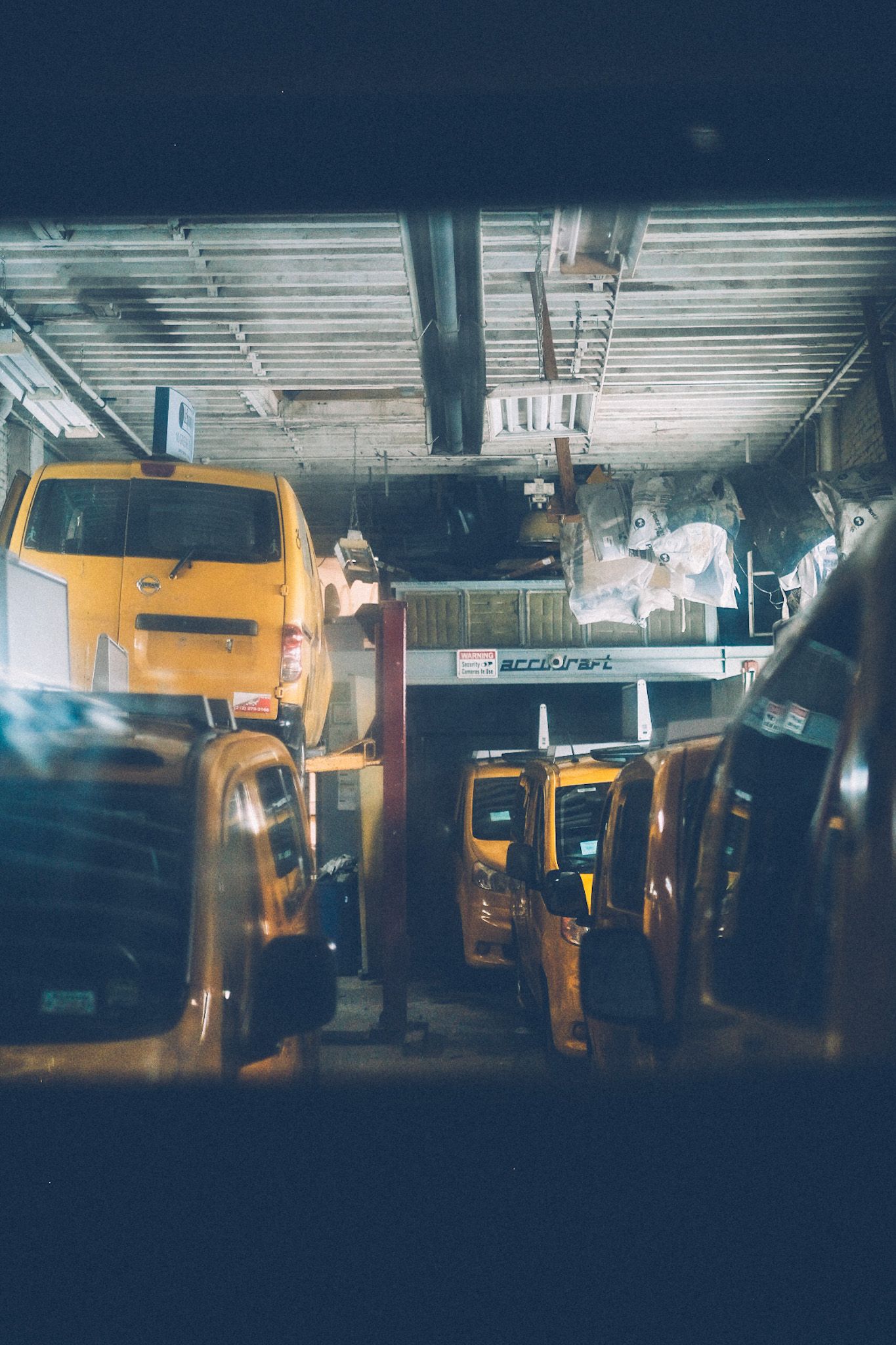 New York taxi cabs sit in a garage together, lit with fluorescent lamps.