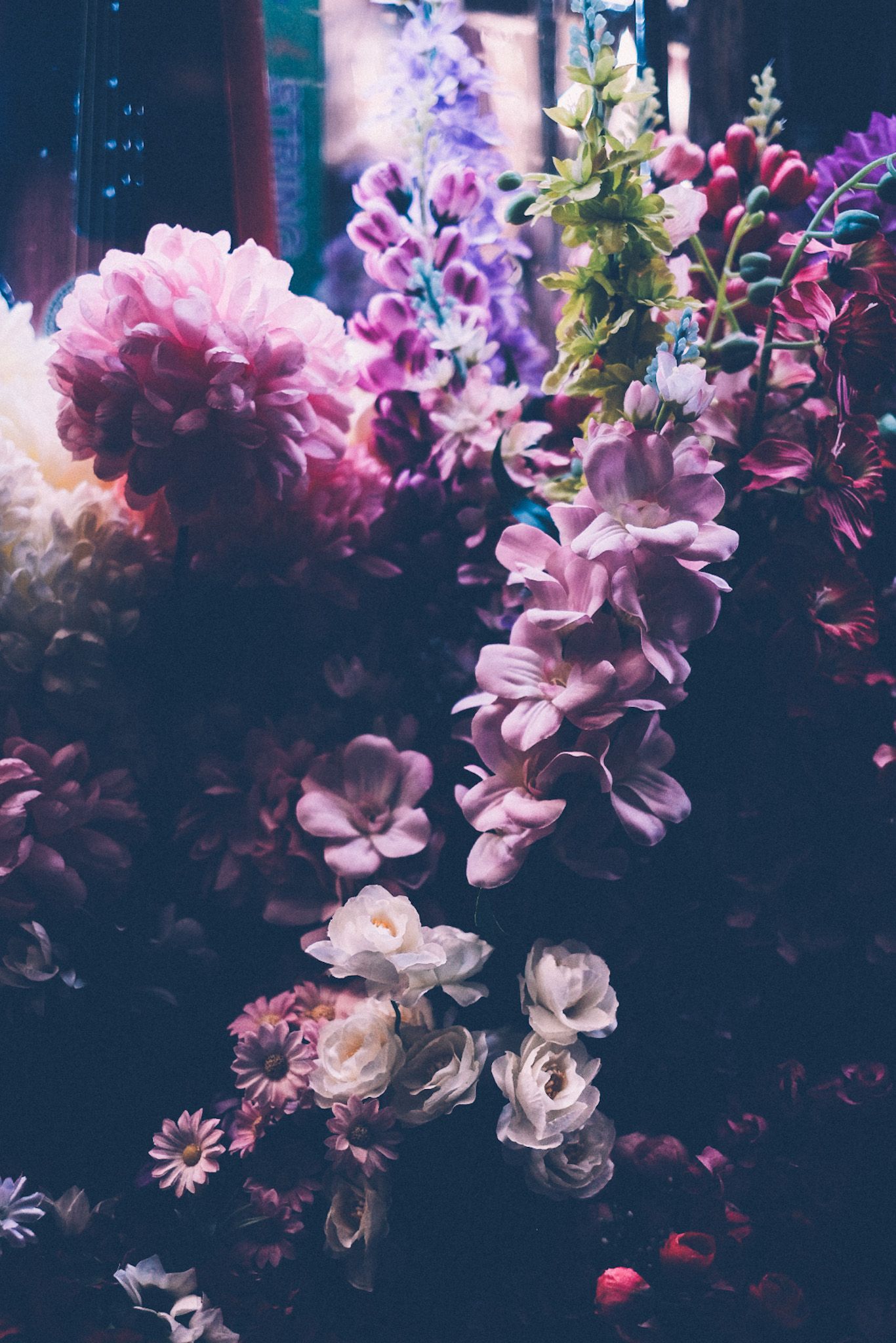 Fake flowers in colors of pink and purple and milky white show under fluorescent night lighting.