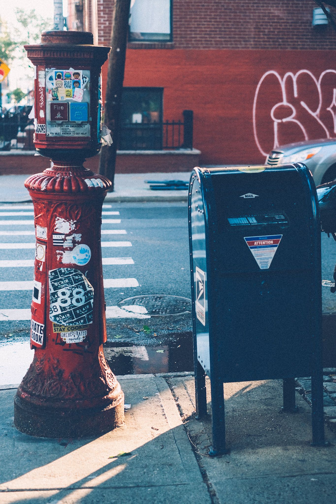 A red signpost and a mailbox sit on the corner of a sidewalk in the morning light.