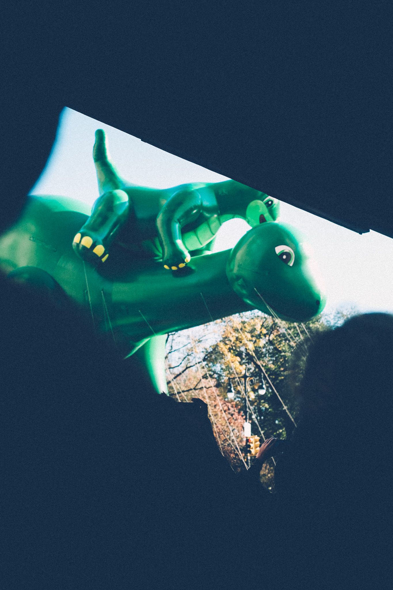 A green dinosaur balloon with a smaller dinosaur balloon on its back floats in the Macy’s Thanksgiving Day Parade.