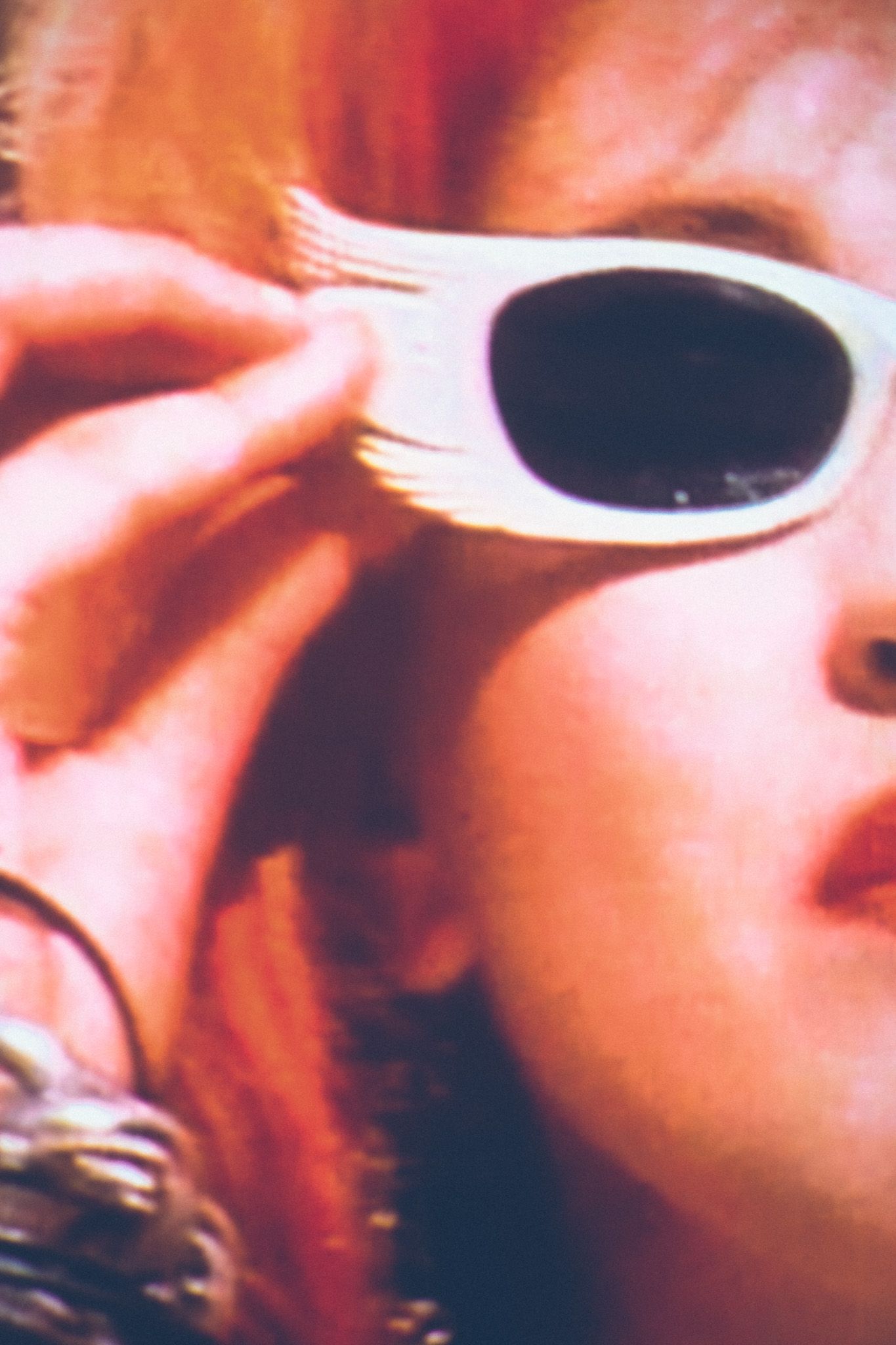 A closeup crop of Cyndi Lauper’s video for Girls Just Want to Have Fun, showing half of her face as she puts on white rimmed sunglasses.