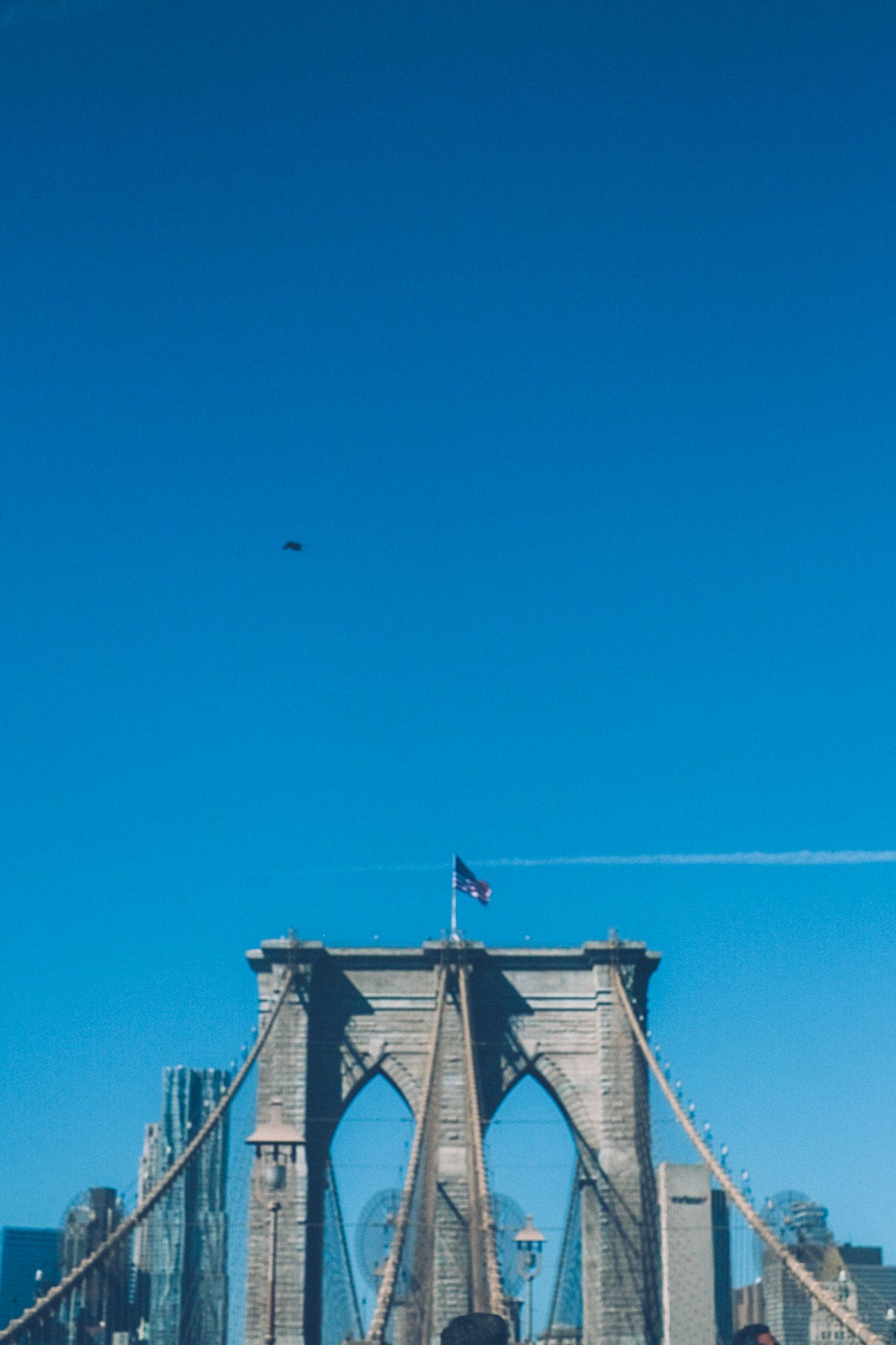 The Brooklyn Bridge rises from the bottom of the frame against a clear blue sky.