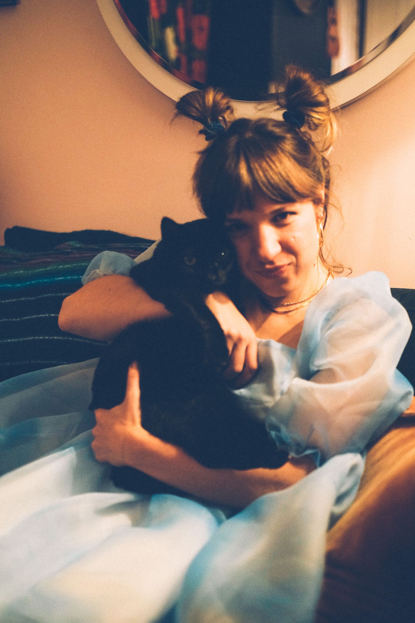 A woman with pigtails in a puffy blue dress sits on a couch, holding a black cat.