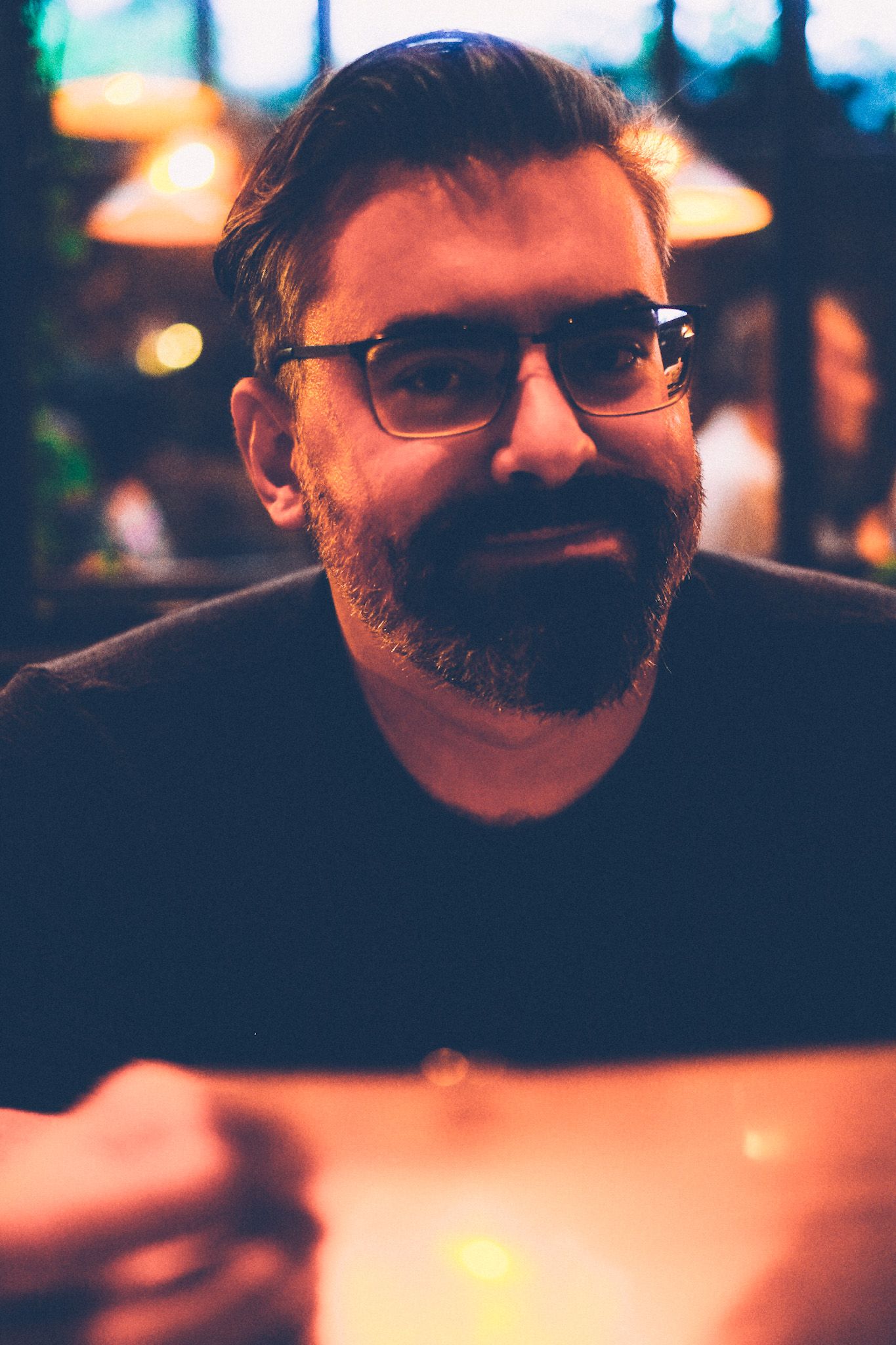 In a dimly lit restaurant, a photo of a bearded man, smiling.