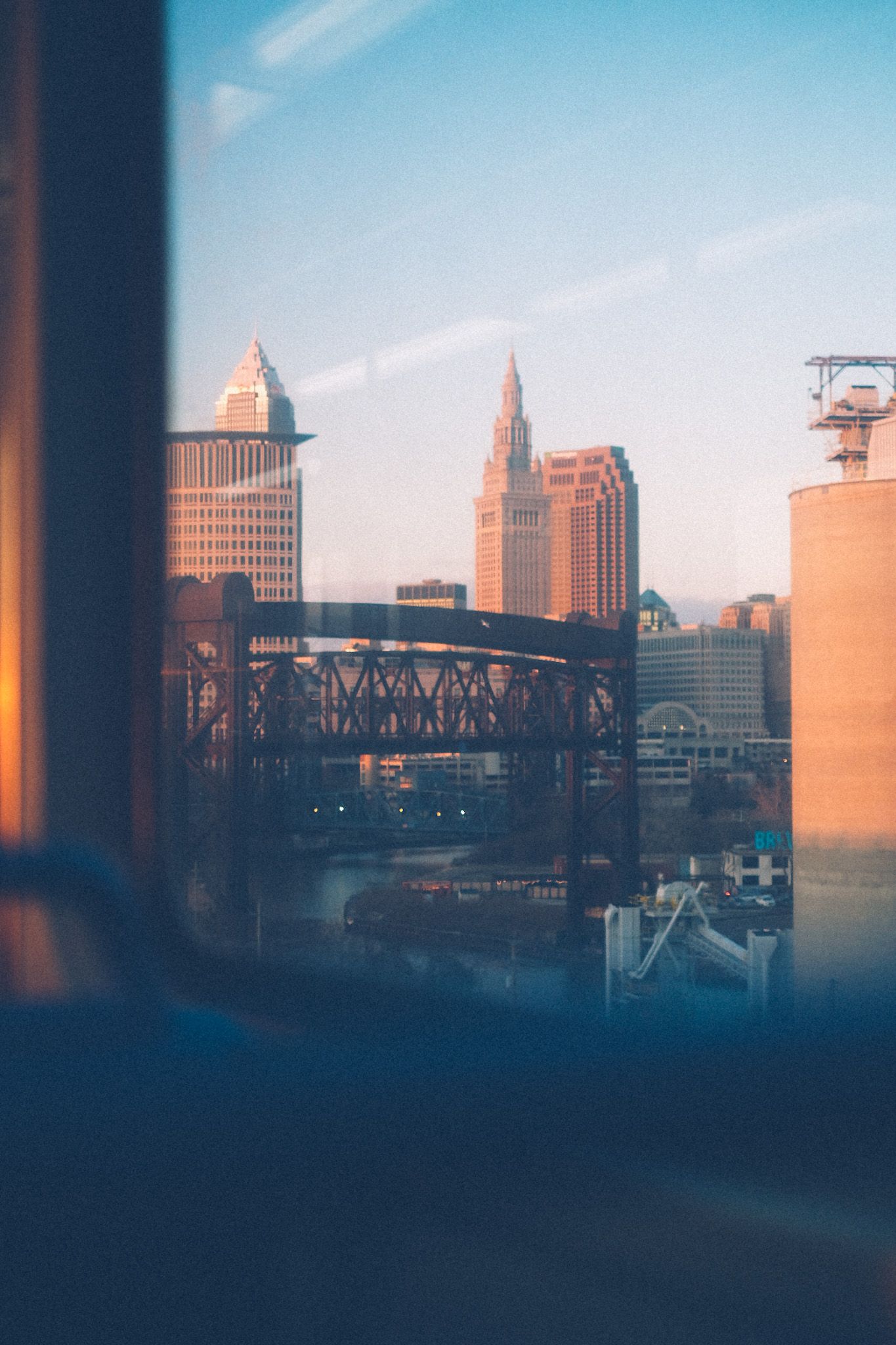 The skyline of downtown Cleveland glimmers in the sunlight from inside the train. A few buildings and a bridge appear in layers.