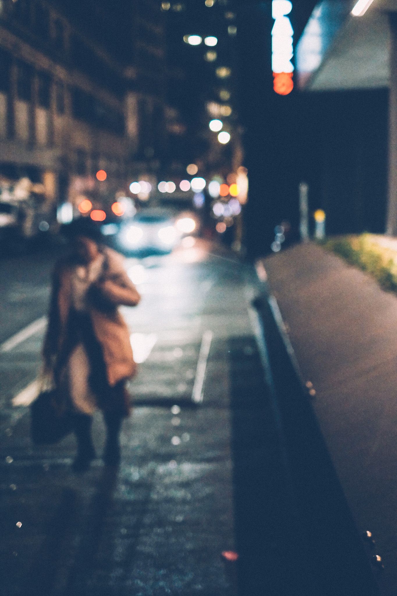Out of focus, a woman runs down a city street at night, car and building lights illuminating the background.