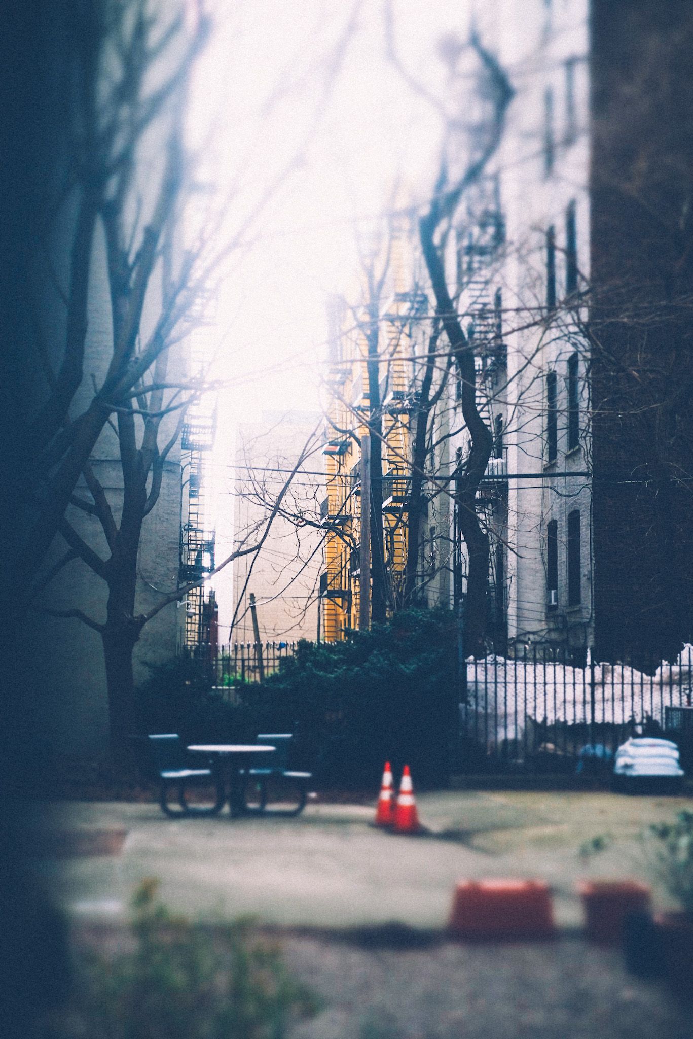 A view of a courtyard, tight depth of field, on a cloudy day. A few orange traffic cones stand in the middle.