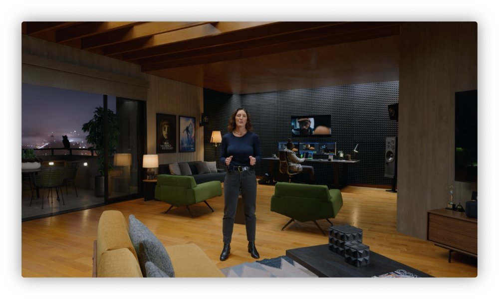 Apple presenter standing inside an apartment while somebody sits at a computer behind her. 