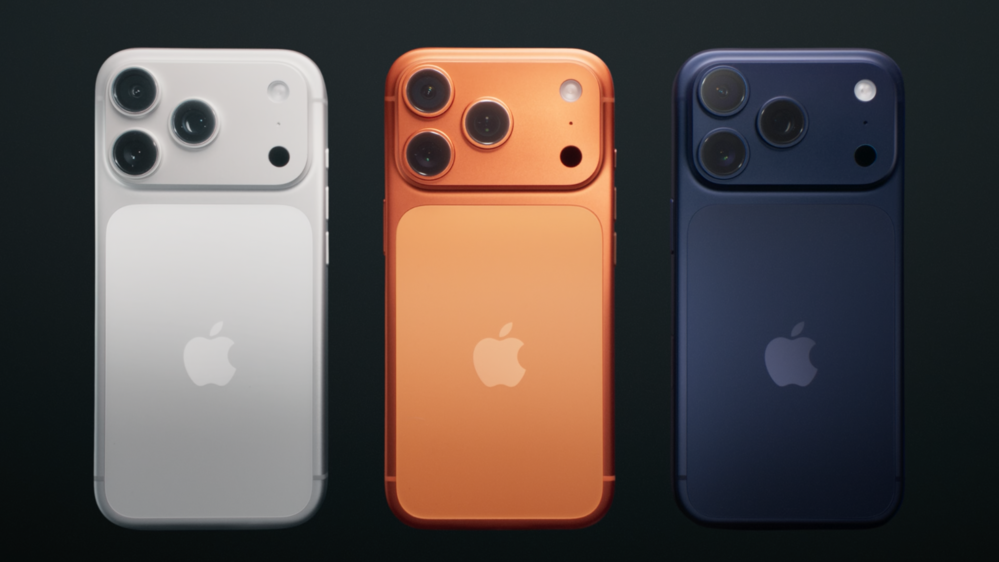 Three smartphones displayed against a black background. From left to right: a white phone, an orange phone, and a dark blue phone. Each phone features a prominent camera module with three lenses and the Apple logo on the back.