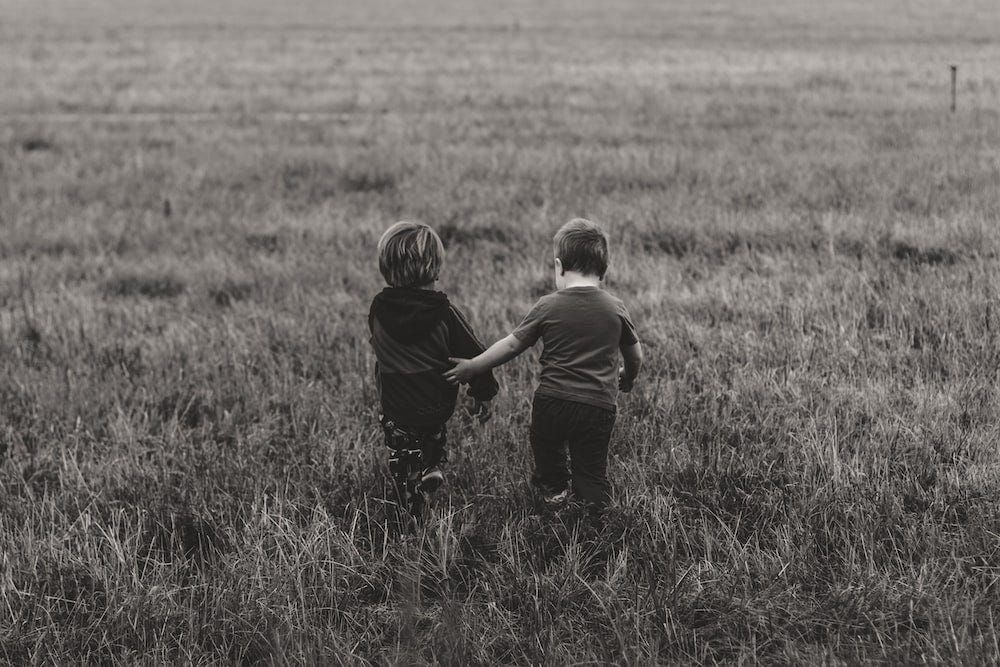 Photo of two children holding hands whilst walking over grass.