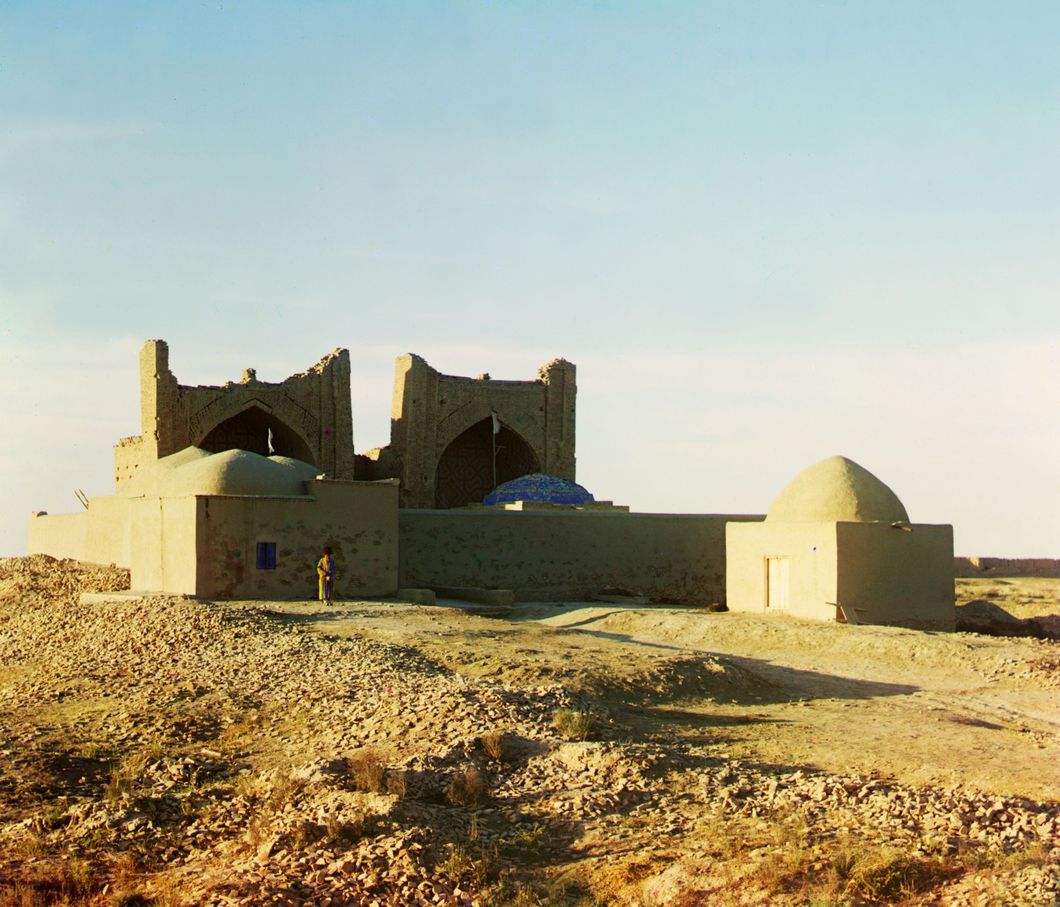 Walled adobe structure with domes and arches in desert area, with man posed in front