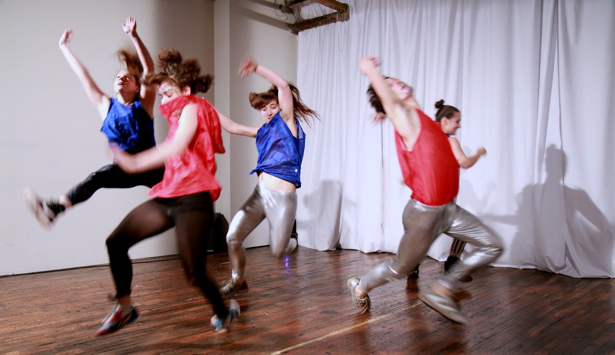 Five young dancers wearing blue and red pennies and vibrant tights are falling to the floor