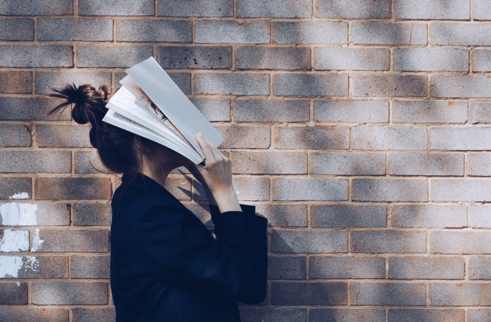 A woman is covering her face with a white book