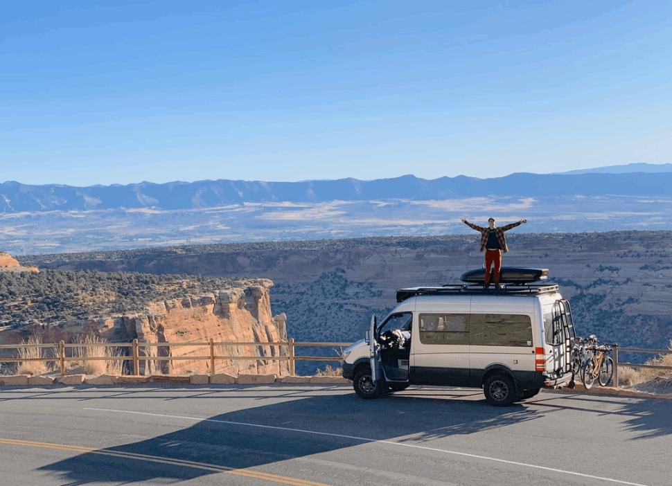 man standing on sprinter van roof by mountain view
