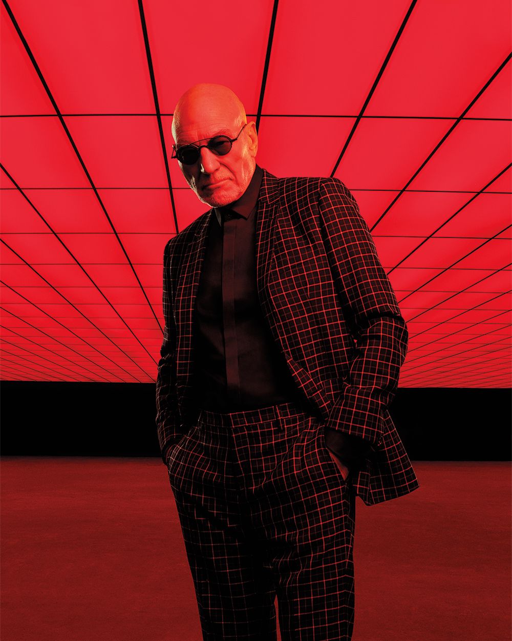 Patrick Stewart in a black suit with a red windowpane check. He is wearing sunglasses.