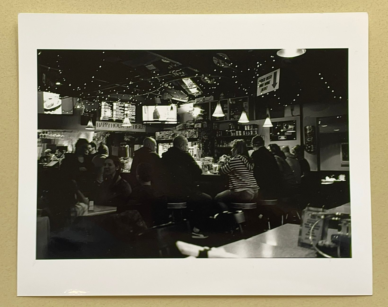 A glossy paper print of a black and white image of customers sitting around the bar and at tables at FireWorks Pizza in Leesburg, Virgina