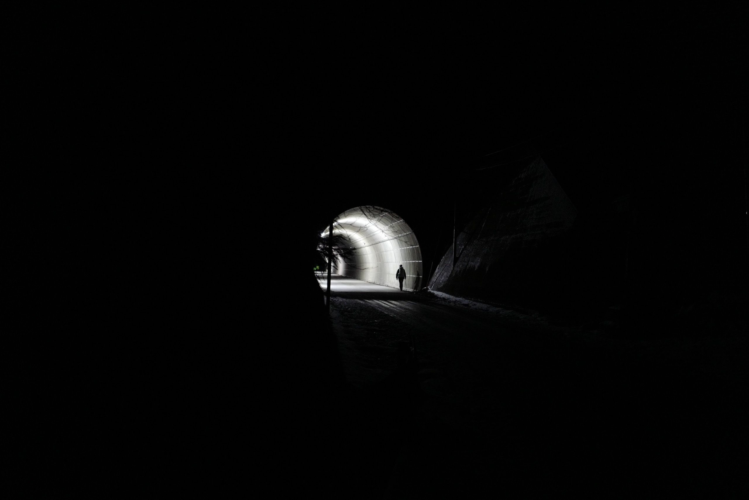 In the distance, a man walks into a tunnel in otherwise complete darkness.